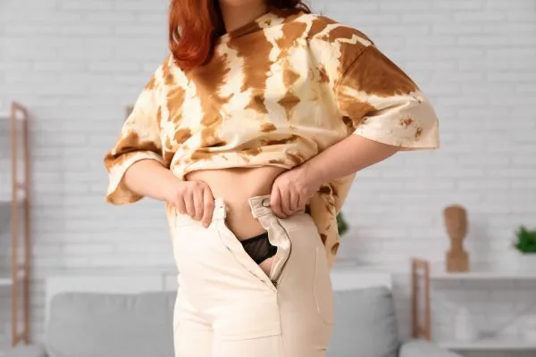 Image of woman trying to do her trousers up after pregnancy weight gain Trowbridge